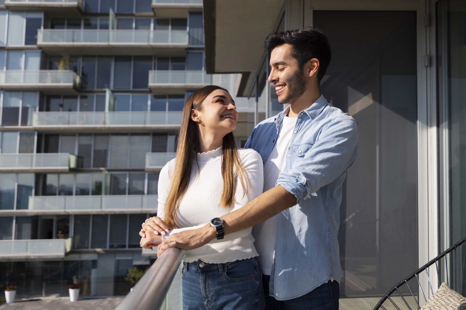 Casal sorridente abraçado em varanda de apartamento após manutenção residencial.